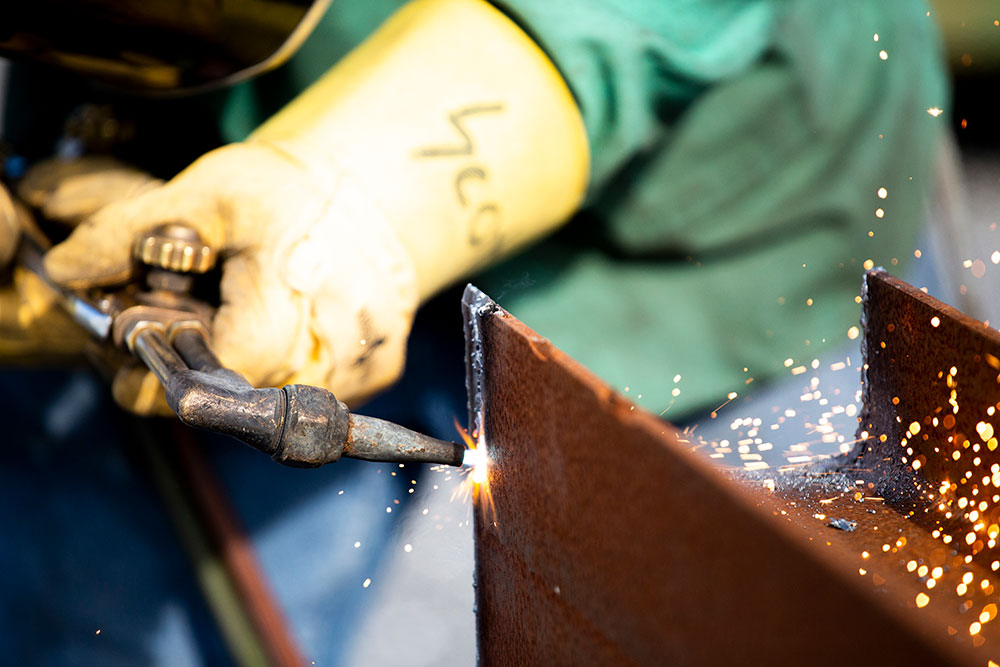 close up of an industrial worker with yellow safety gloves welding a metal part