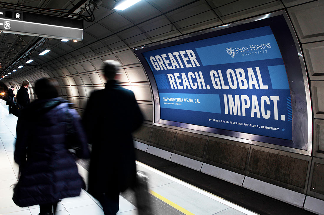 A sample advertisement in a Washington, D.C. Metro Station. Commuters are walking hurriedly past an ad that reads 'Greater Reach. Global Impact.'