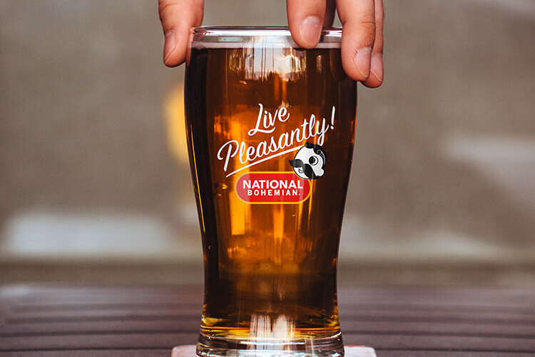 A pint glass full of beer features the “Live Pleasantly!