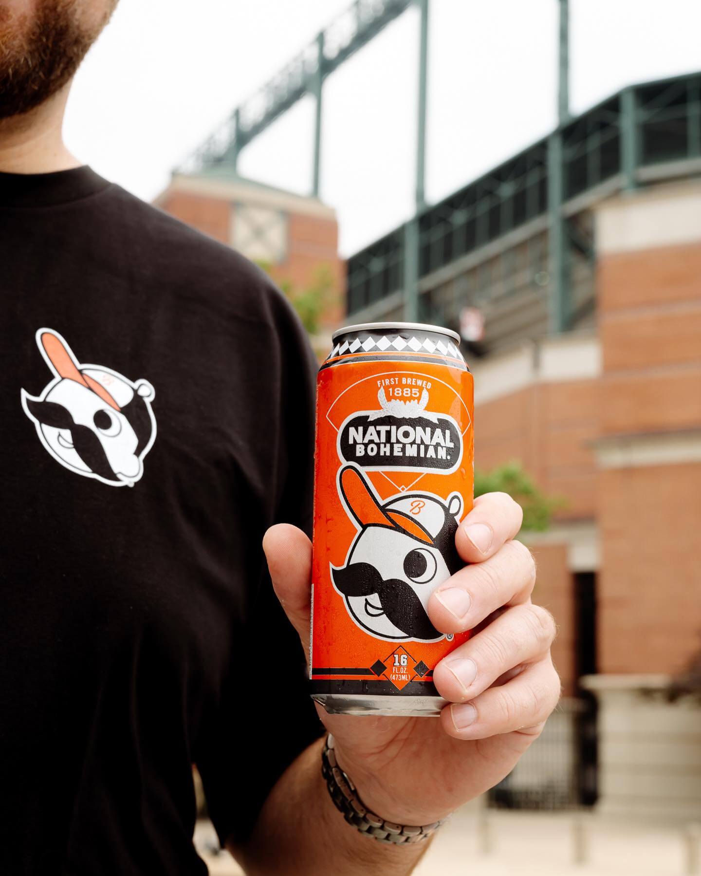 A photo of a man holding a National Bohemian beer can outside of Oriole Park at Camden Yards in Baltimore.