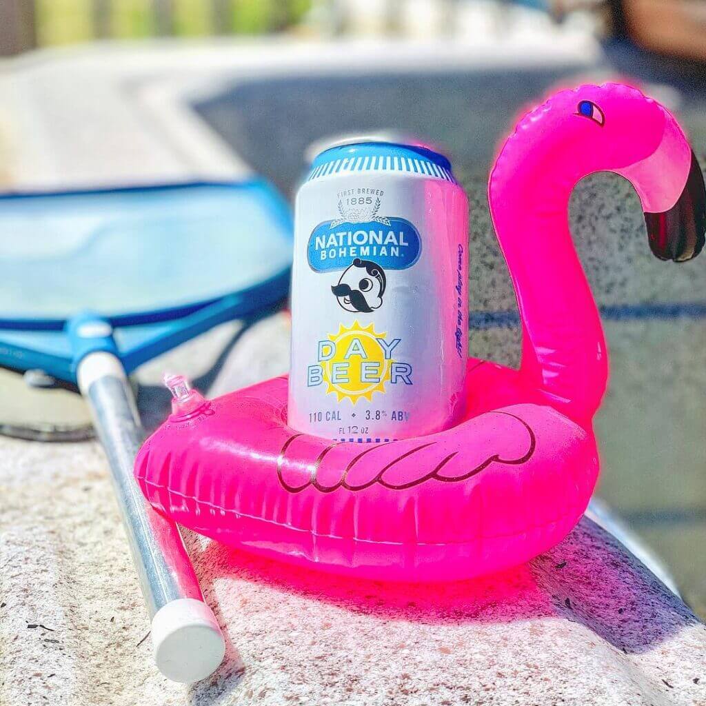 A close-up shot of Day Beer in a miniature inflatable flamingo cup holder intended to resemble a pool float.
