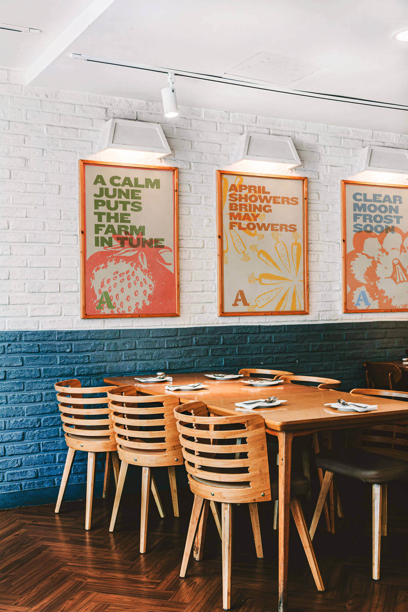 Dining table with six seats against white and blue brick wall with framed Atwater’s prints