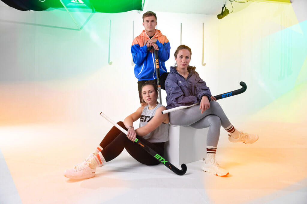 Three field hockey players pose together in a studio.
