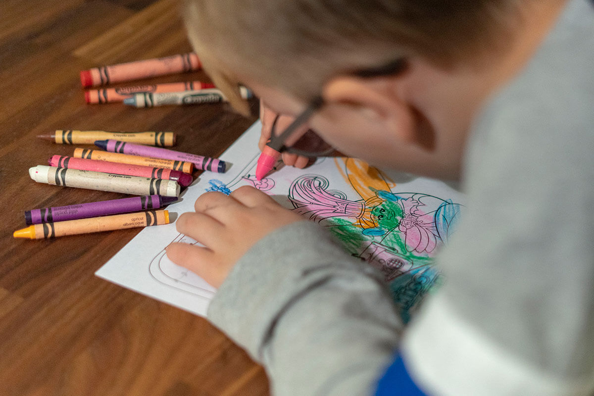 A child colors on a Trolls coloring book page.