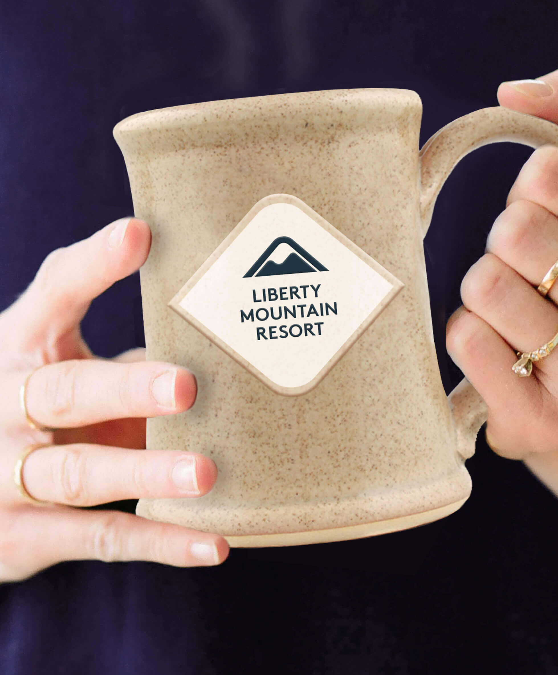 Woman’s hands holding a branded ceramic mug.