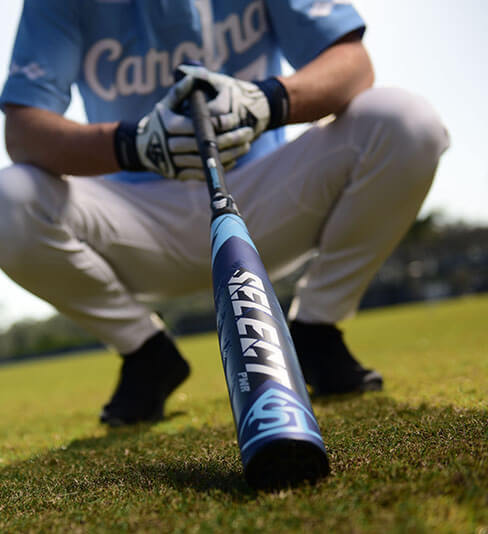 A crouching male baseball player extends his bat toward the camera, revealing the bat artwork.