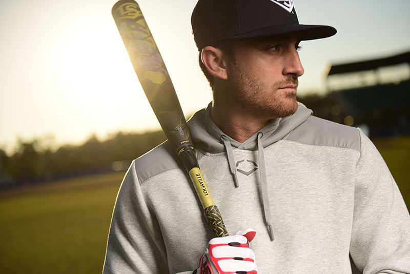 A male baseball player in casual clothes holds a baseball bat against his shoulder. He gazes longingly into the distance. One may surmise he’s daydreaming of hot summer nights, roaring crowds, and glory on the diamond.