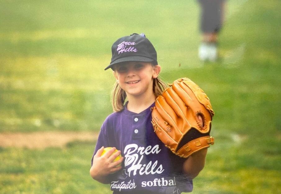 Aubree Munro as a child wearing a Brea Hills softball uniform, hat, and glove.