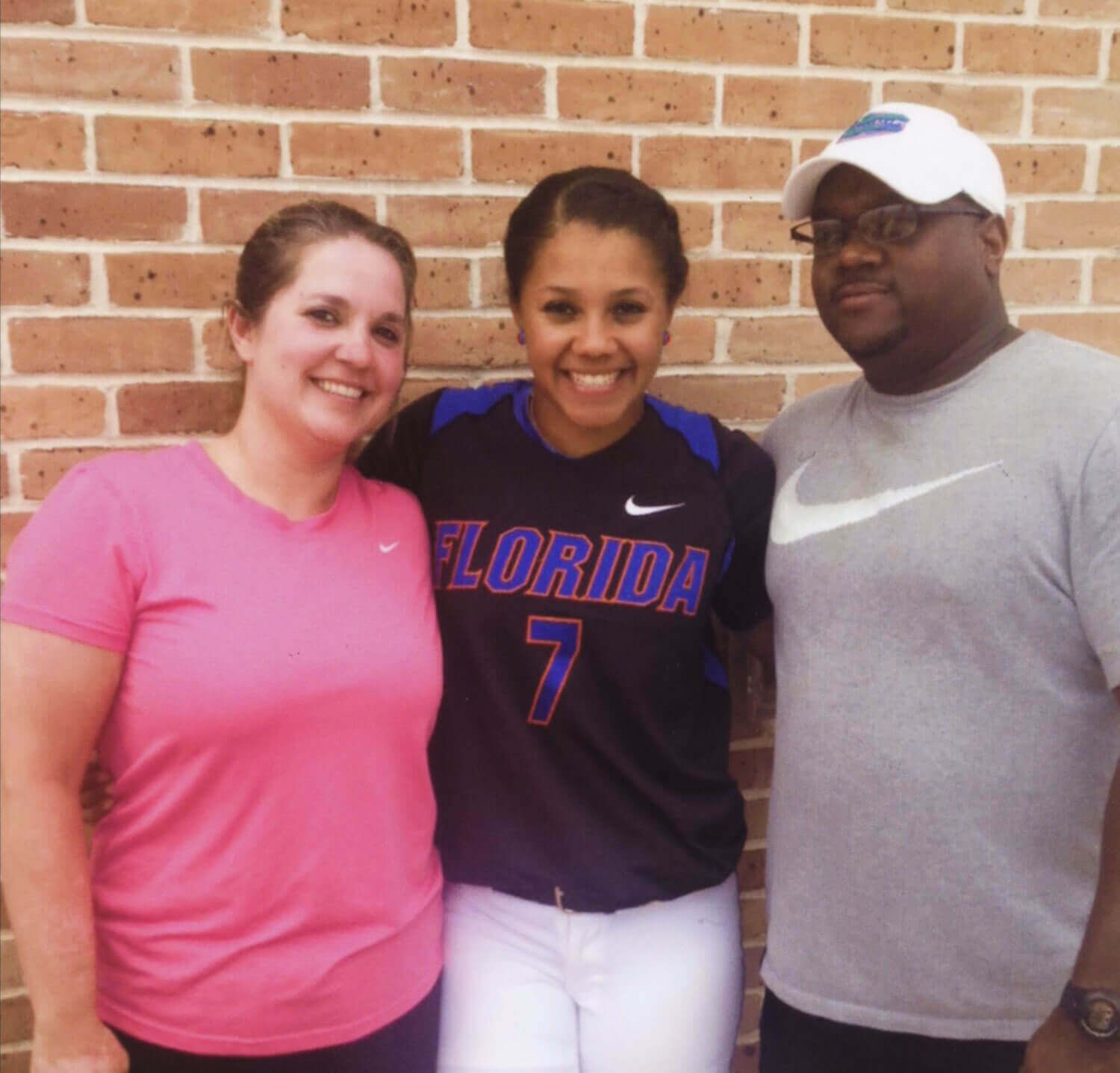 A photo of Kelsey Stewart in her Florida uniform, with her parents on either side.
