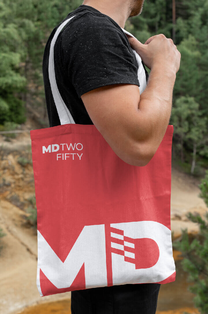 A mocked-up image of a tote bag featuring an abstracted version of the MD TWO FIFTY logo.