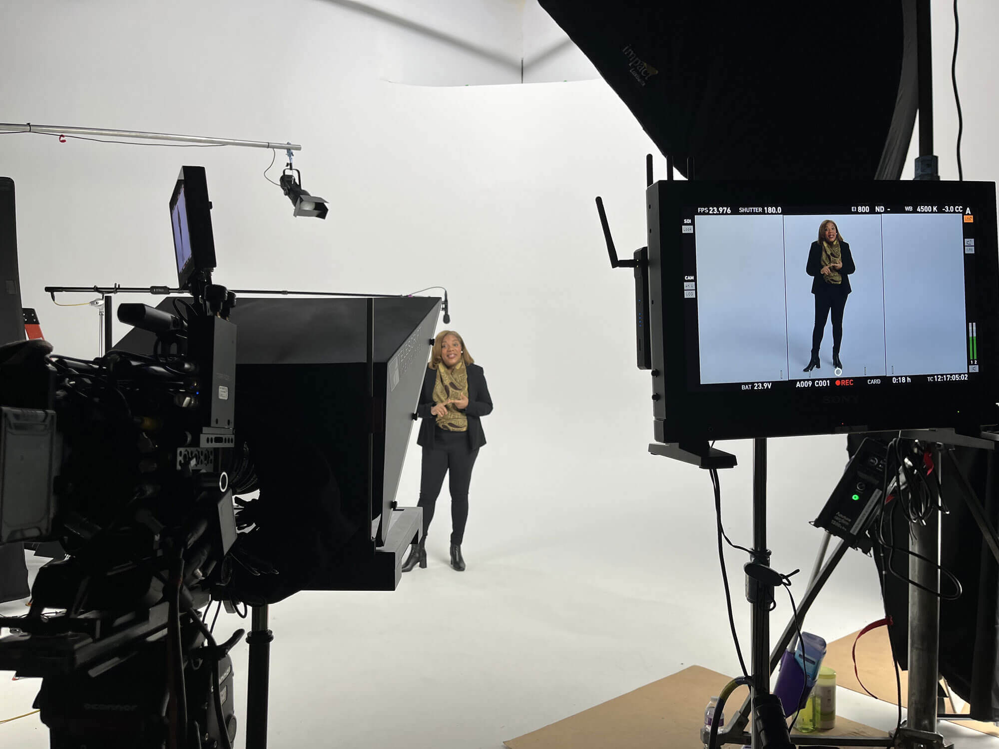 A behind-the-scenes photo from the campaign photoshoot featuring a woman on set, facing a camera and video monitor.