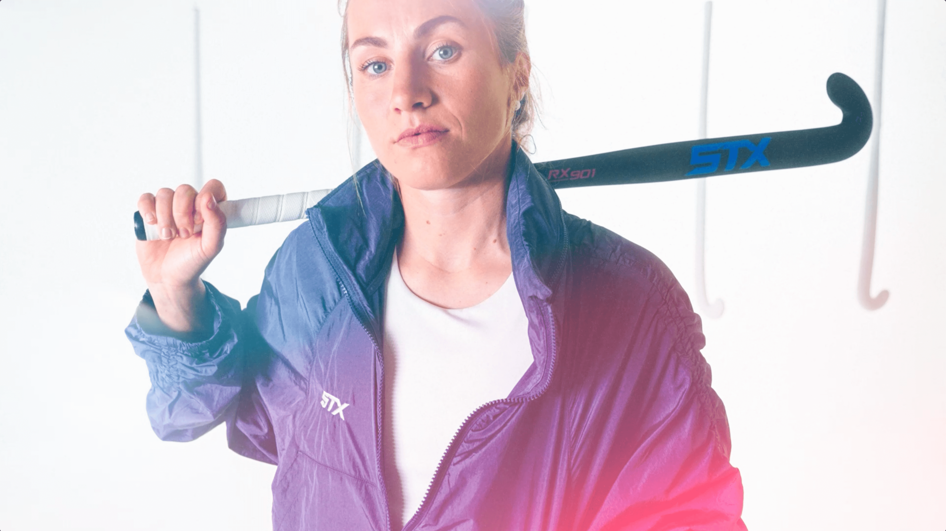 A female field hockey player stylishly poses with a field hockey stick in a studio.