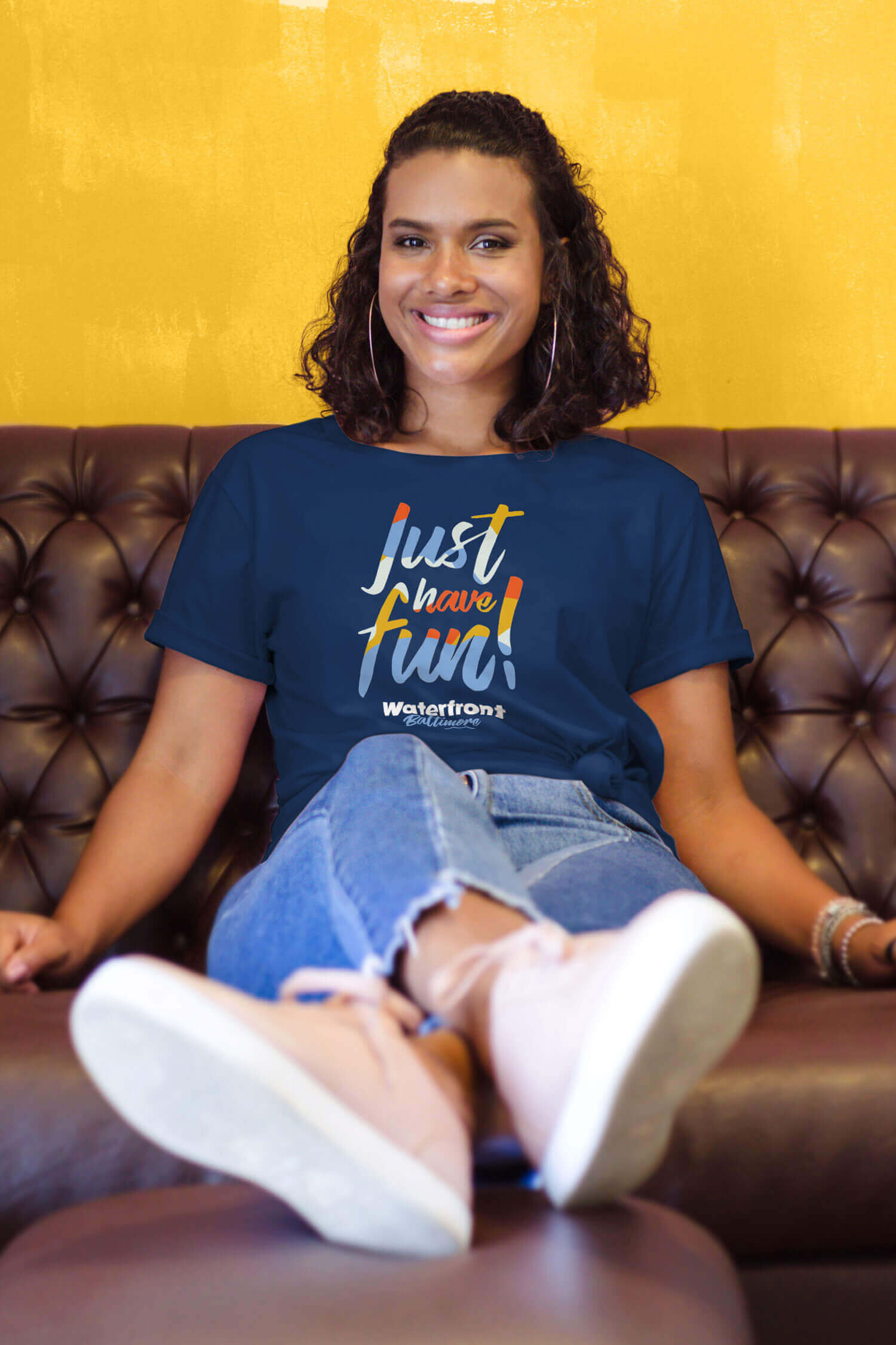 A woman sitting on a couch wearing a Waterfront Baltimore partnership t-shirt.