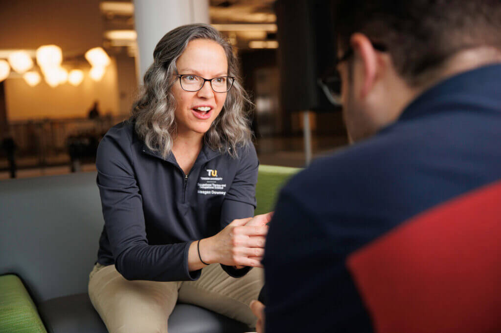 A female physical therapist grad student sits with a patient.