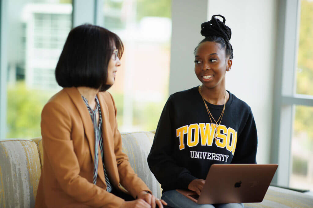 A female grad student sits on a couch with her mentor, a female faculty member.